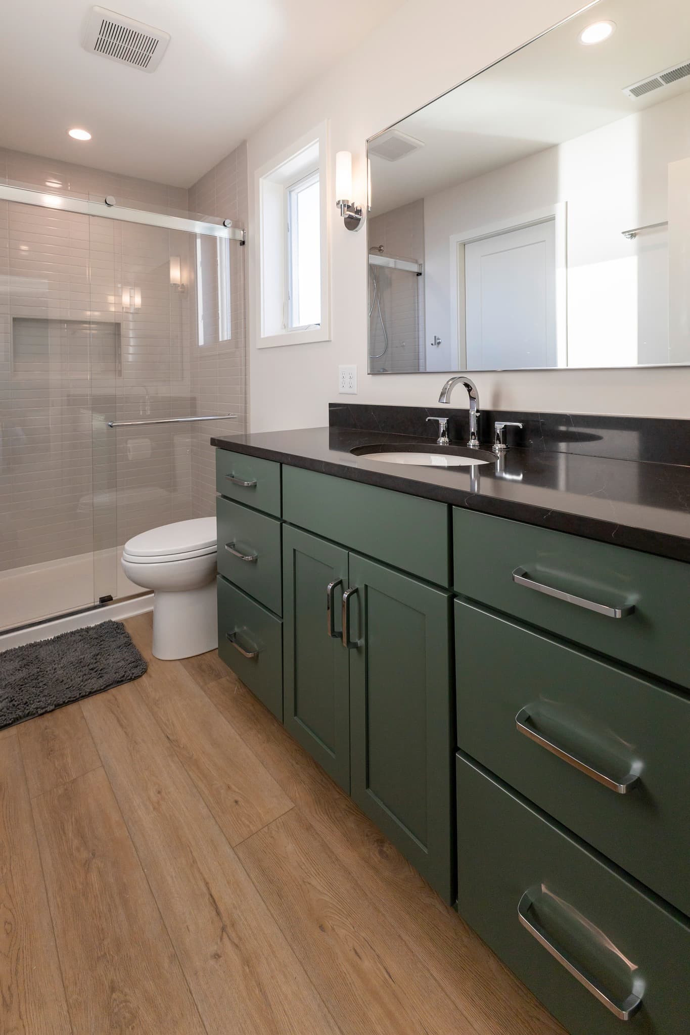 Green vanity with dark countertop and glass-enclosed tub/shower