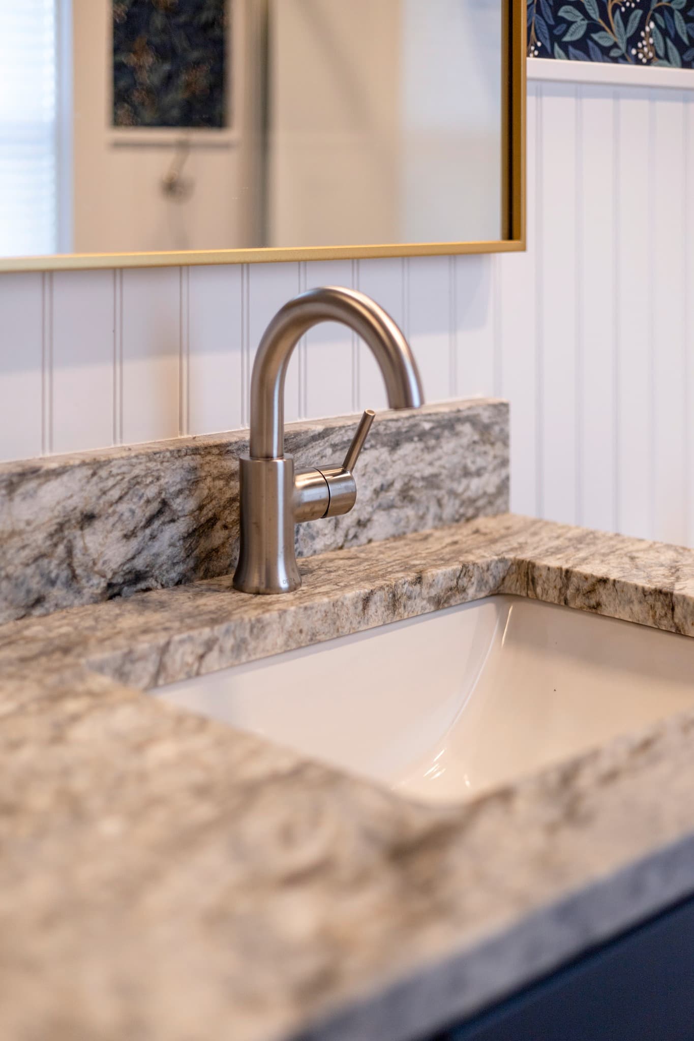 Close-up of brushed nickel faucet on natural stone countertop with beadboard wall