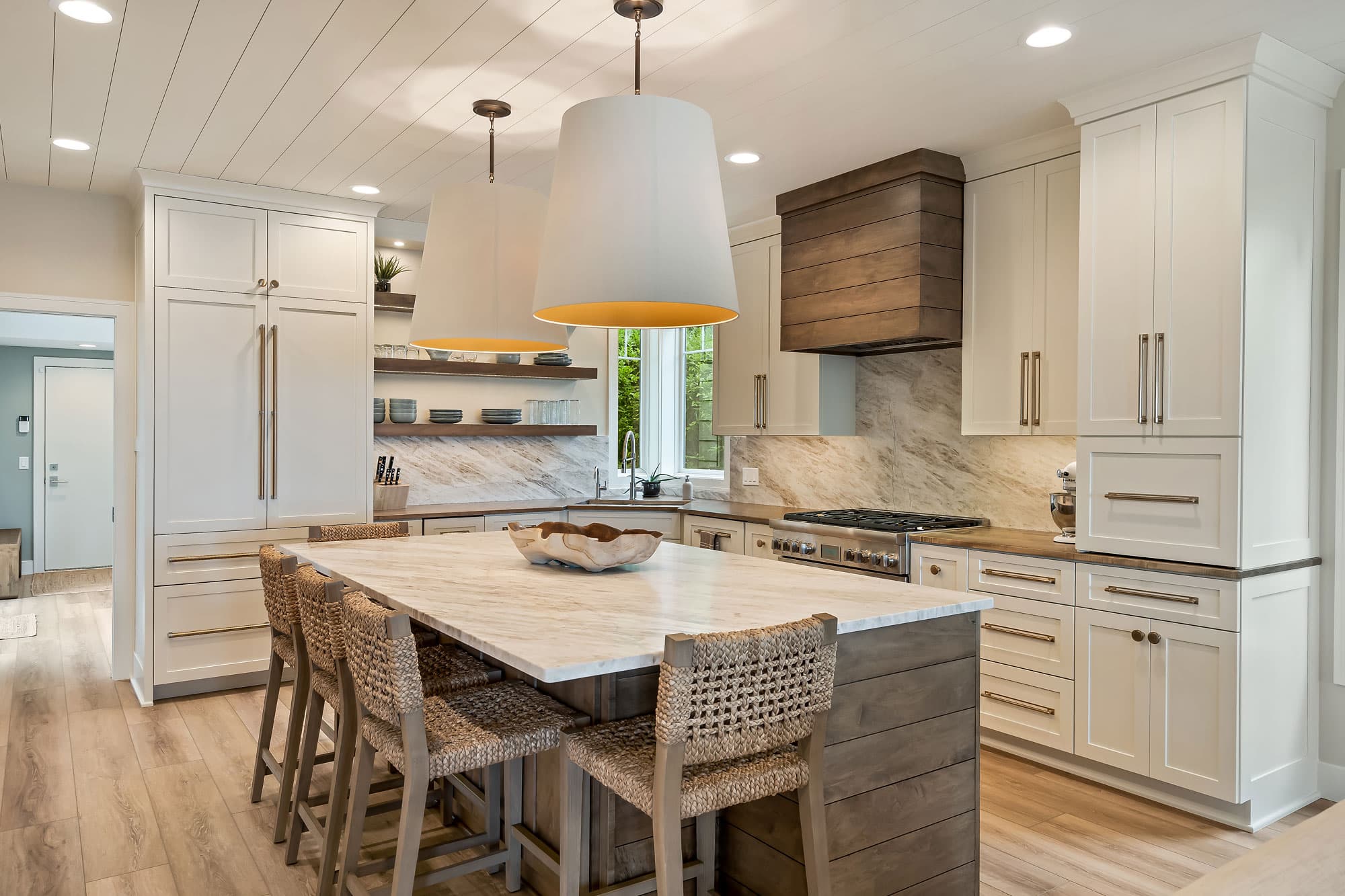 Coastal kitchen with oversized pendants, marble island, and wood hood