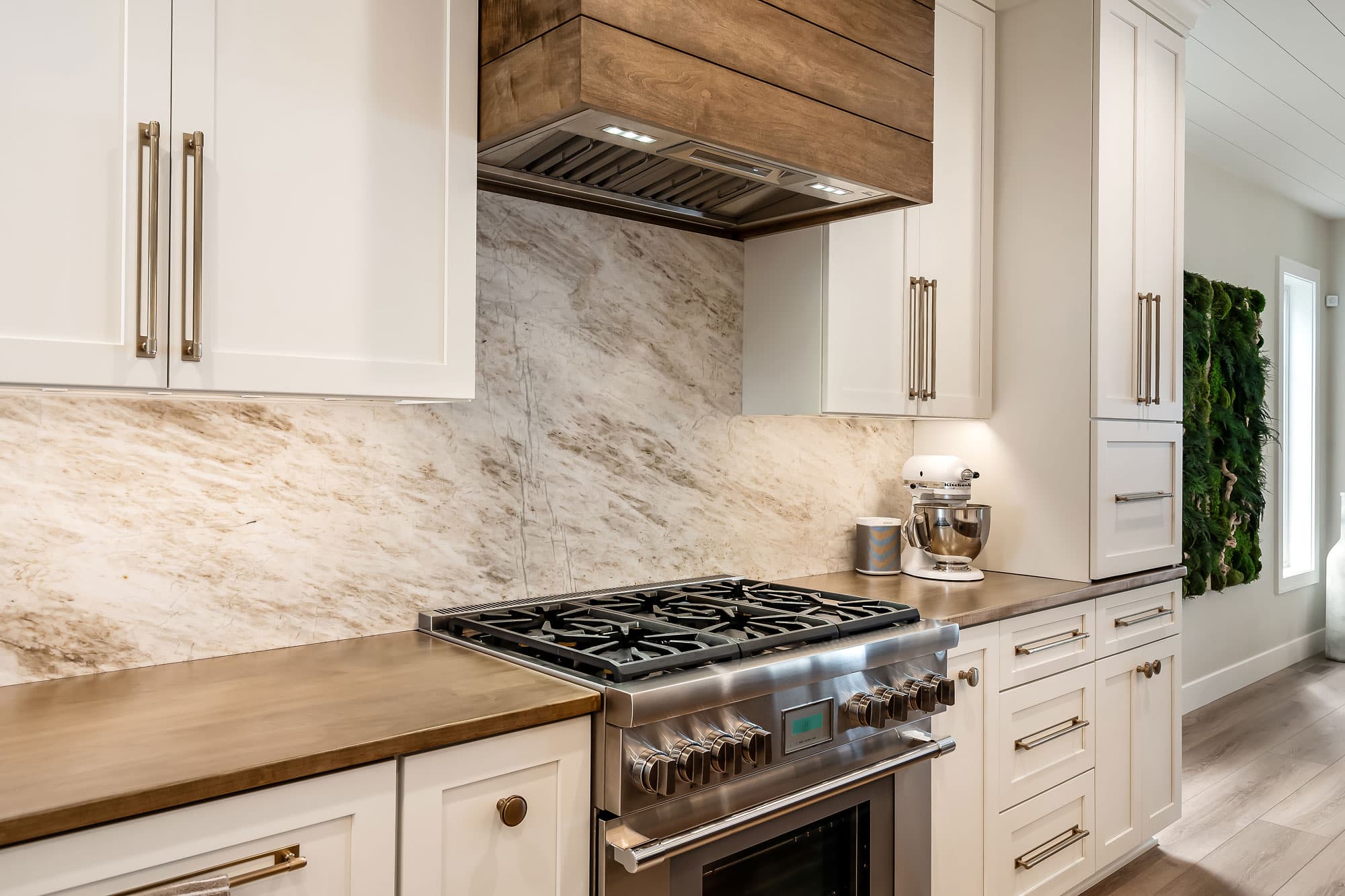 White cabinets with marble backsplash, wood range hood, and butcher block counter