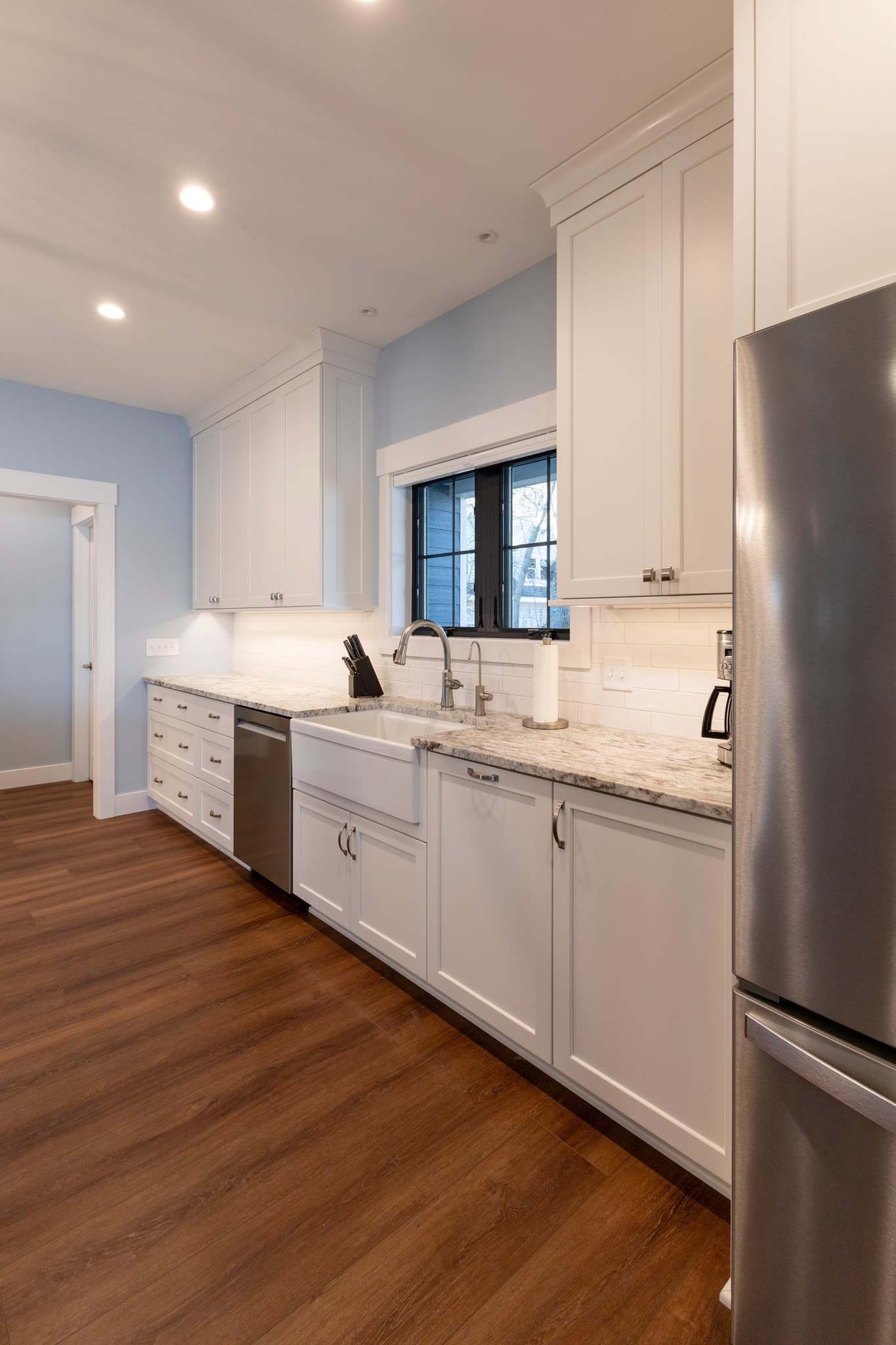 White galley kitchen with farmhouse sink, granite, and blue walls