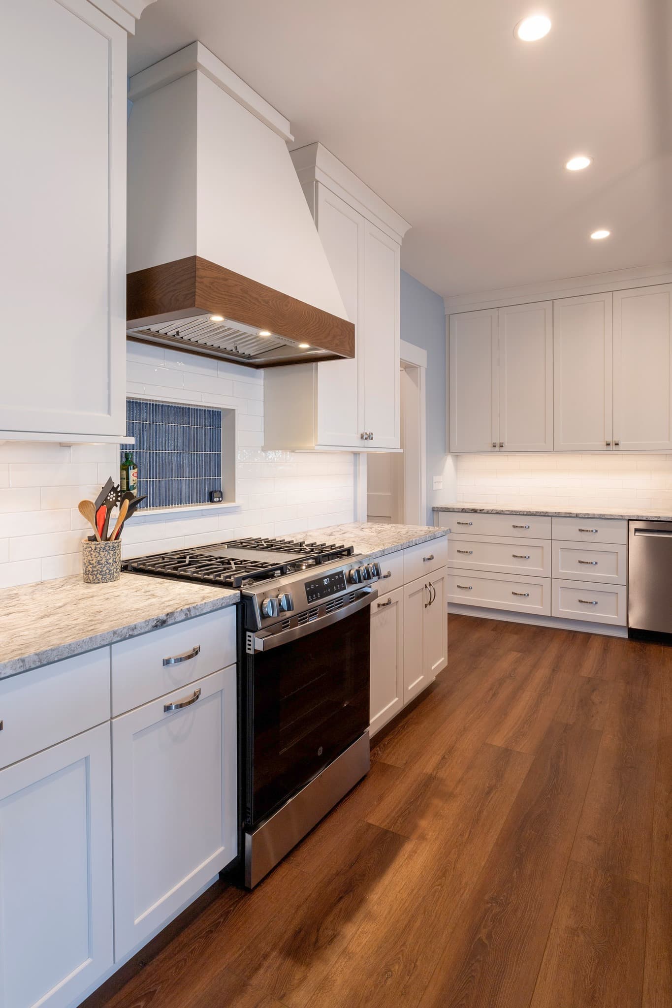 White kitchen with custom range hood, granite countertops, and hardwood floors